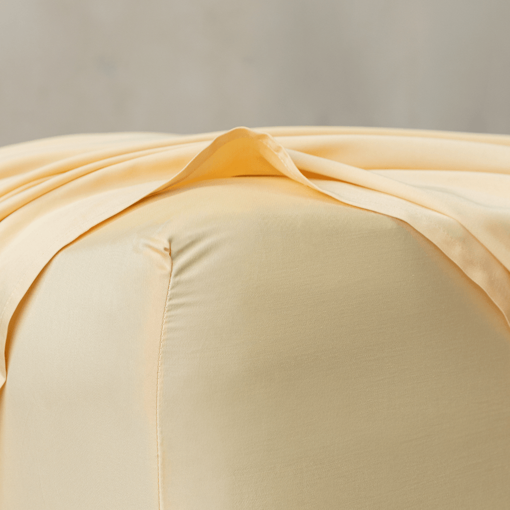 Close-up corner detail of a pale yellow fitted sheet and top flat sheet showing smooth texture and seam stitching