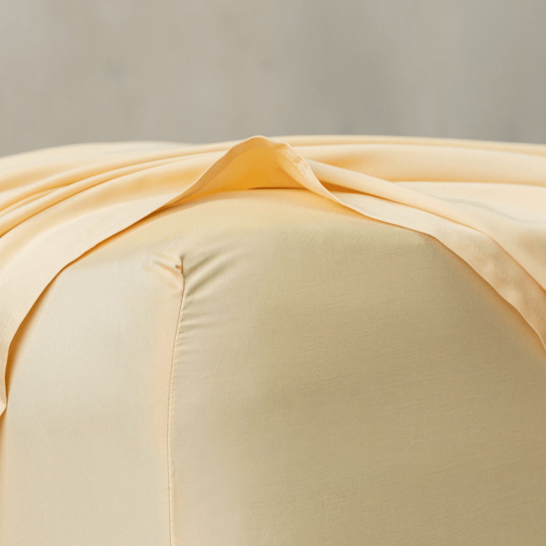 Close-up corner detail of a pale yellow fitted sheet and top flat sheet showing smooth texture and seam stitching