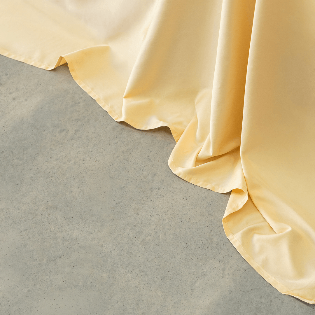 Close-up of pale yellow sheet fabric draping softly onto a light gray floor