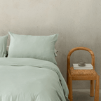 Close-up bedroom styling shot featuring sage green bedding paired with a timber chair, emphasizing the calming color and relaxed texture.