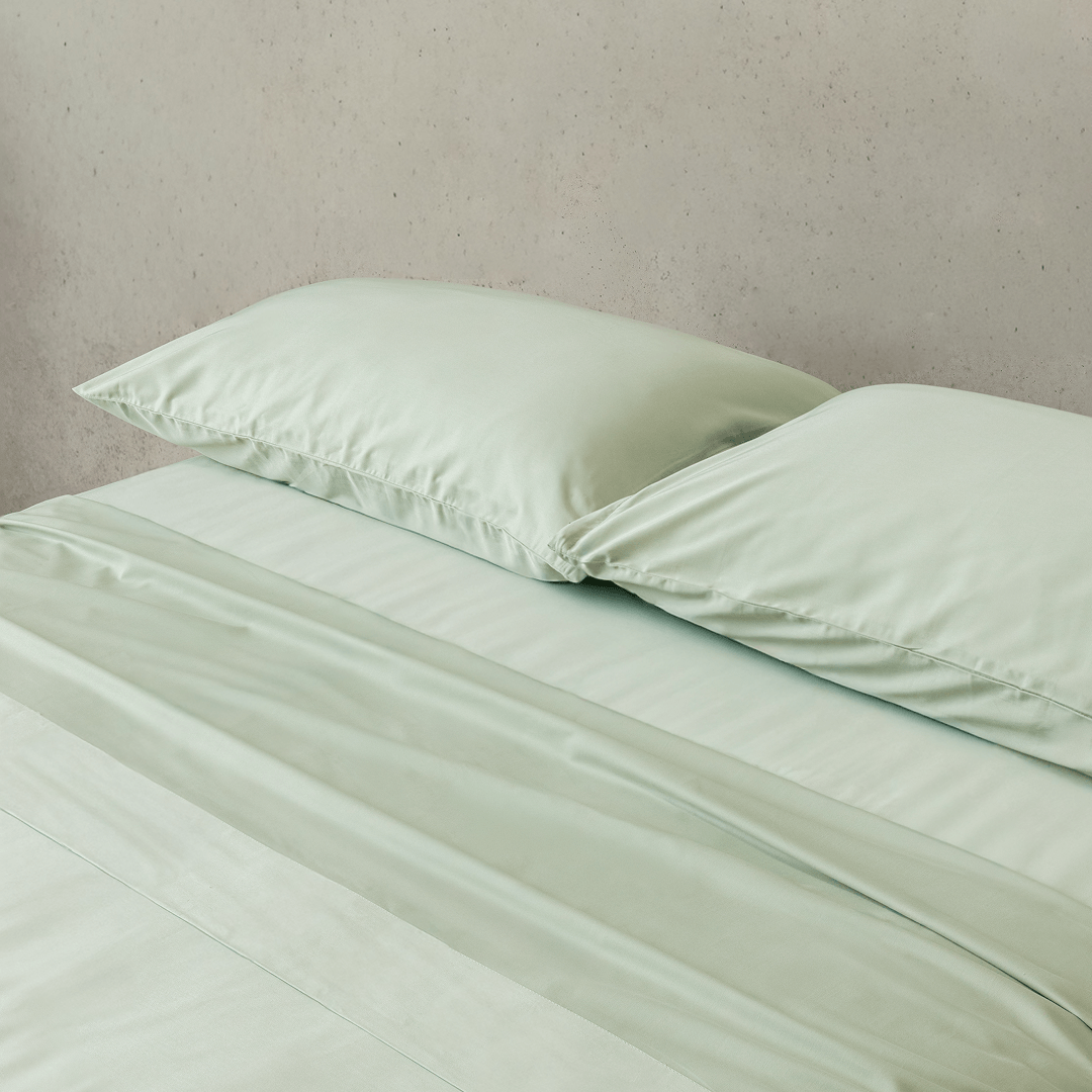 Close-up of matching sage green pillowcases and fitted sheet, highlighting the silky-soft fabric, smooth texture, and coordinated bedding design.