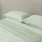 Close-up of matching sage green pillowcases and fitted sheet, highlighting the silky-soft fabric, smooth texture, and coordinated bedding design.