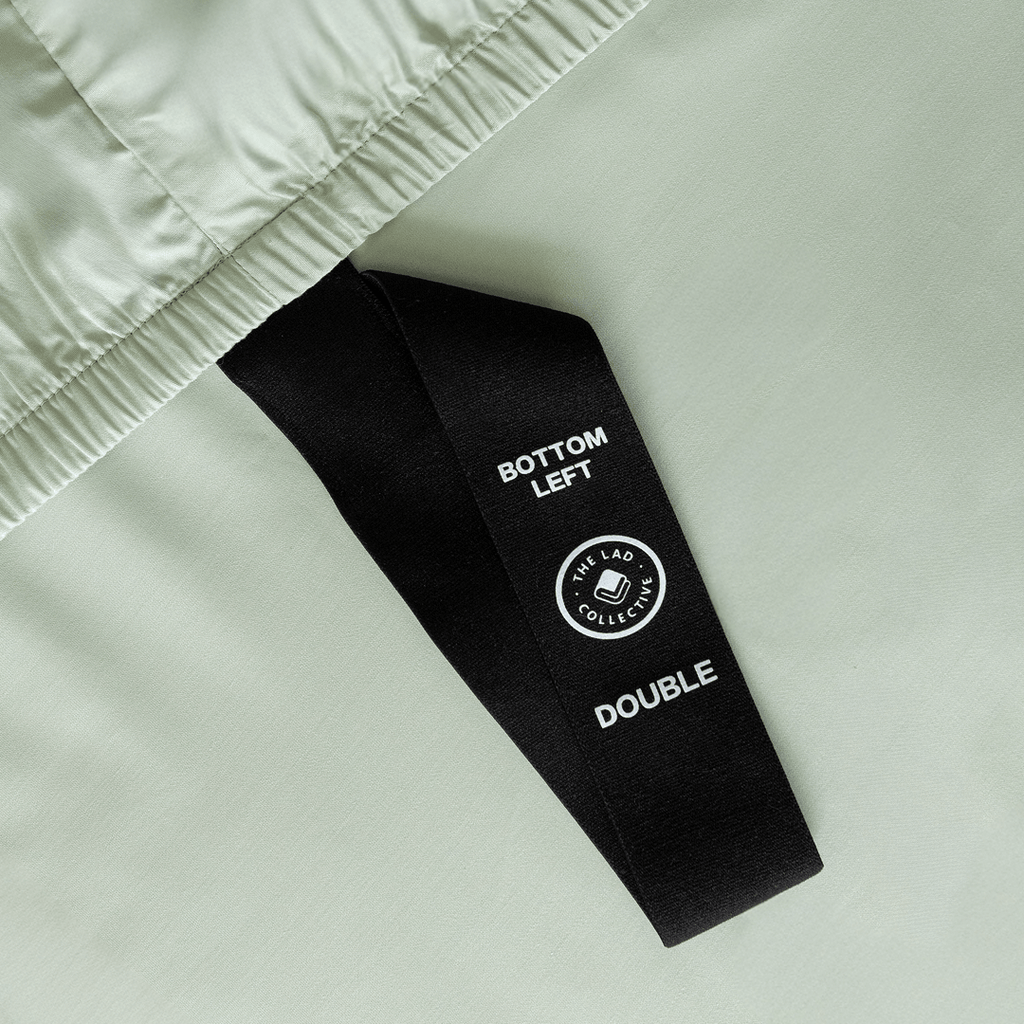 Detailed view of the fitted sheet corner label, showing the size indicator and orientation tag designed for easier bed making.