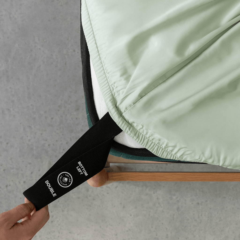 Close-up of the fitted sheet secured around the mattress corner, highlighting the elastic edge and orientation tag for quick installation.