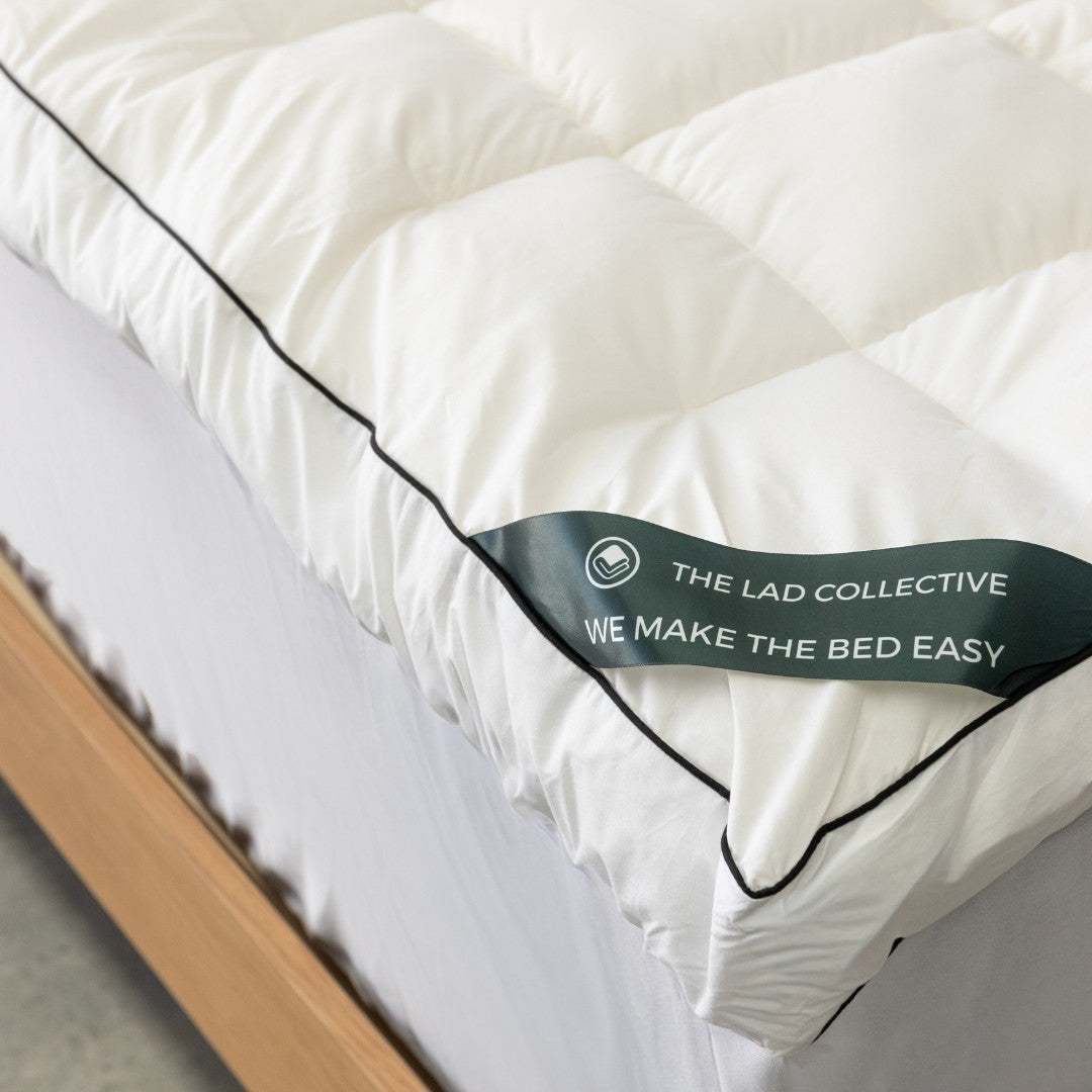 White mattress topper with 'The Lad Collective' label on a bed.