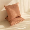 Two clay textured European pillows on a beige surface with soft lighting.