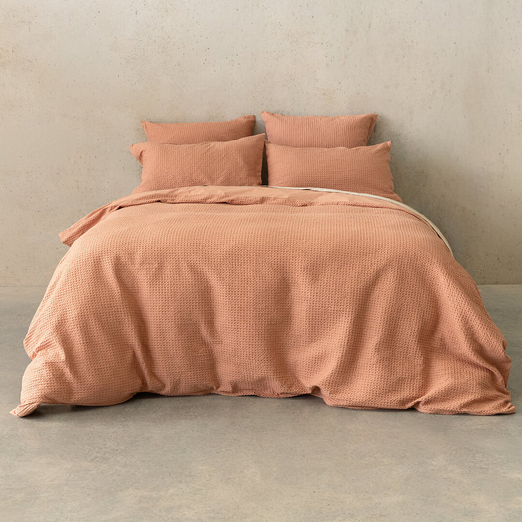 Pink textured bedspread with matching pillows on a bed against a neutral wall.