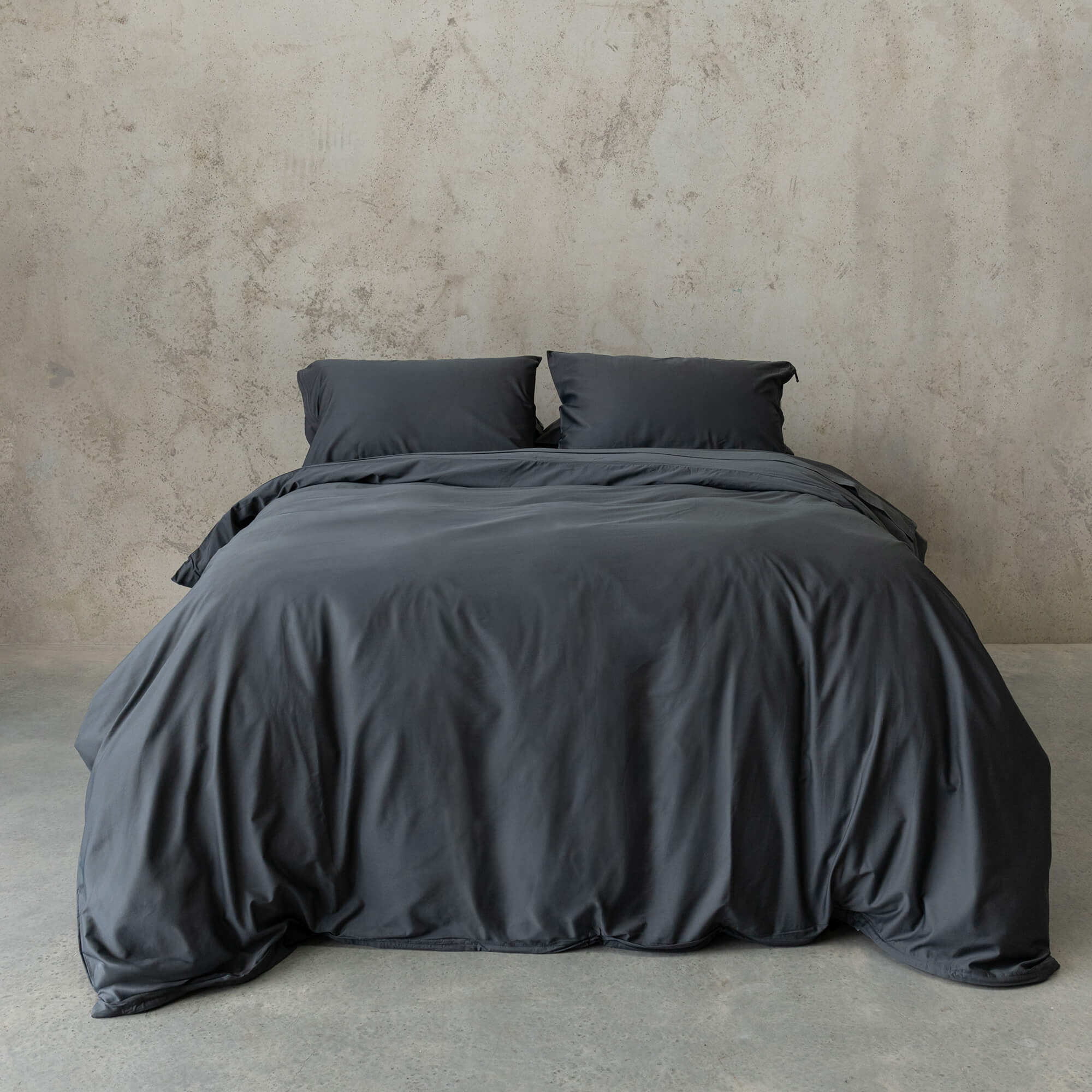 Dark grey bedding set on a bed against a plain wall.
