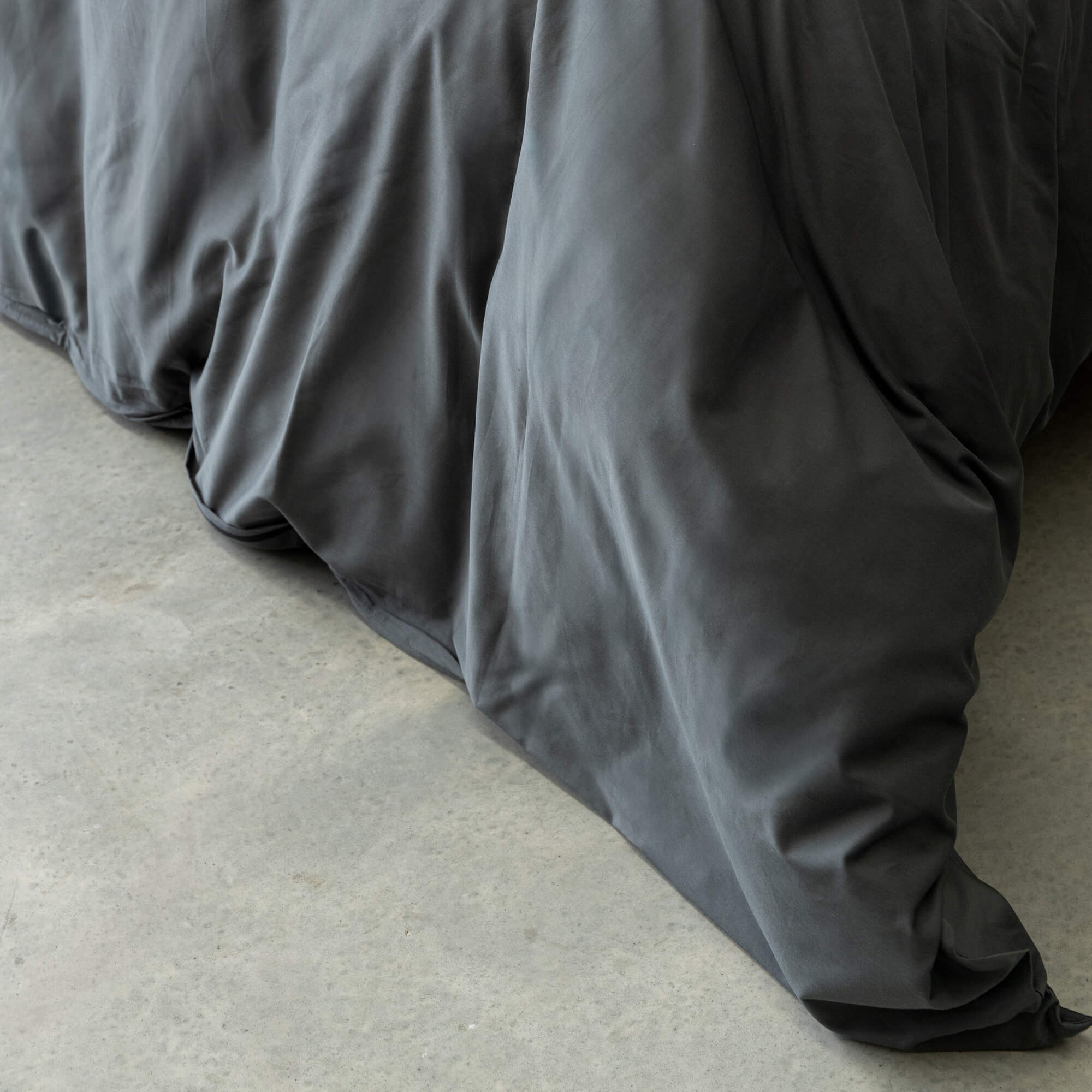 Dark gray comforter on a bed with a neutral background