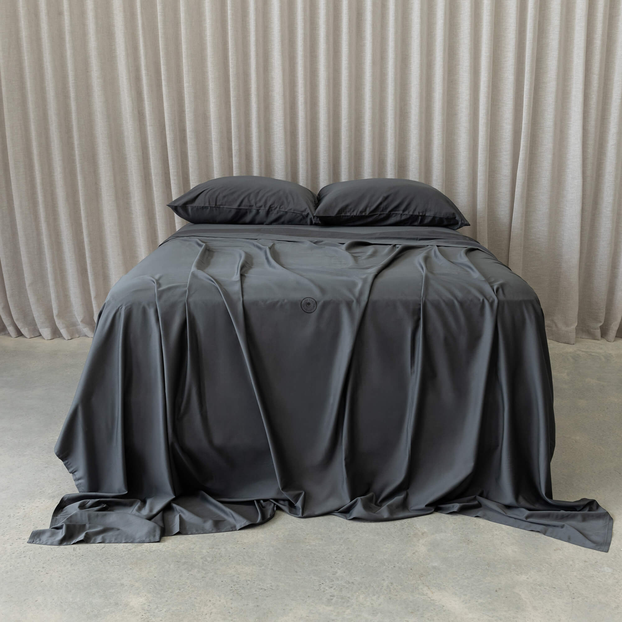 Grey bedspread on a bed with pillows against a beige curtain background