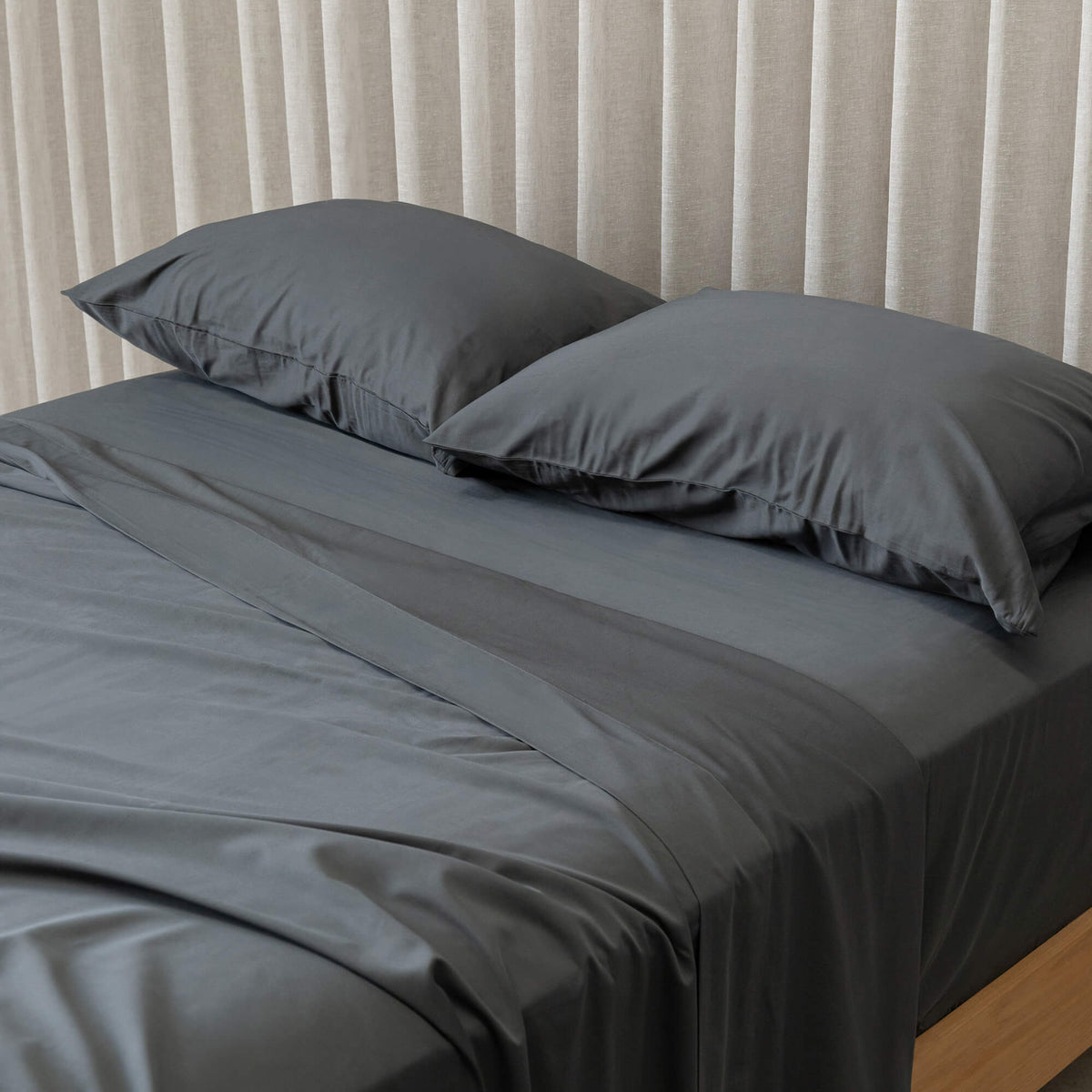 Grey bedspread on a bed with pillows against a beige curtain background