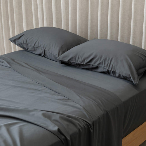 Grey bedding set with two pillows on a bed against a neutral curtain background