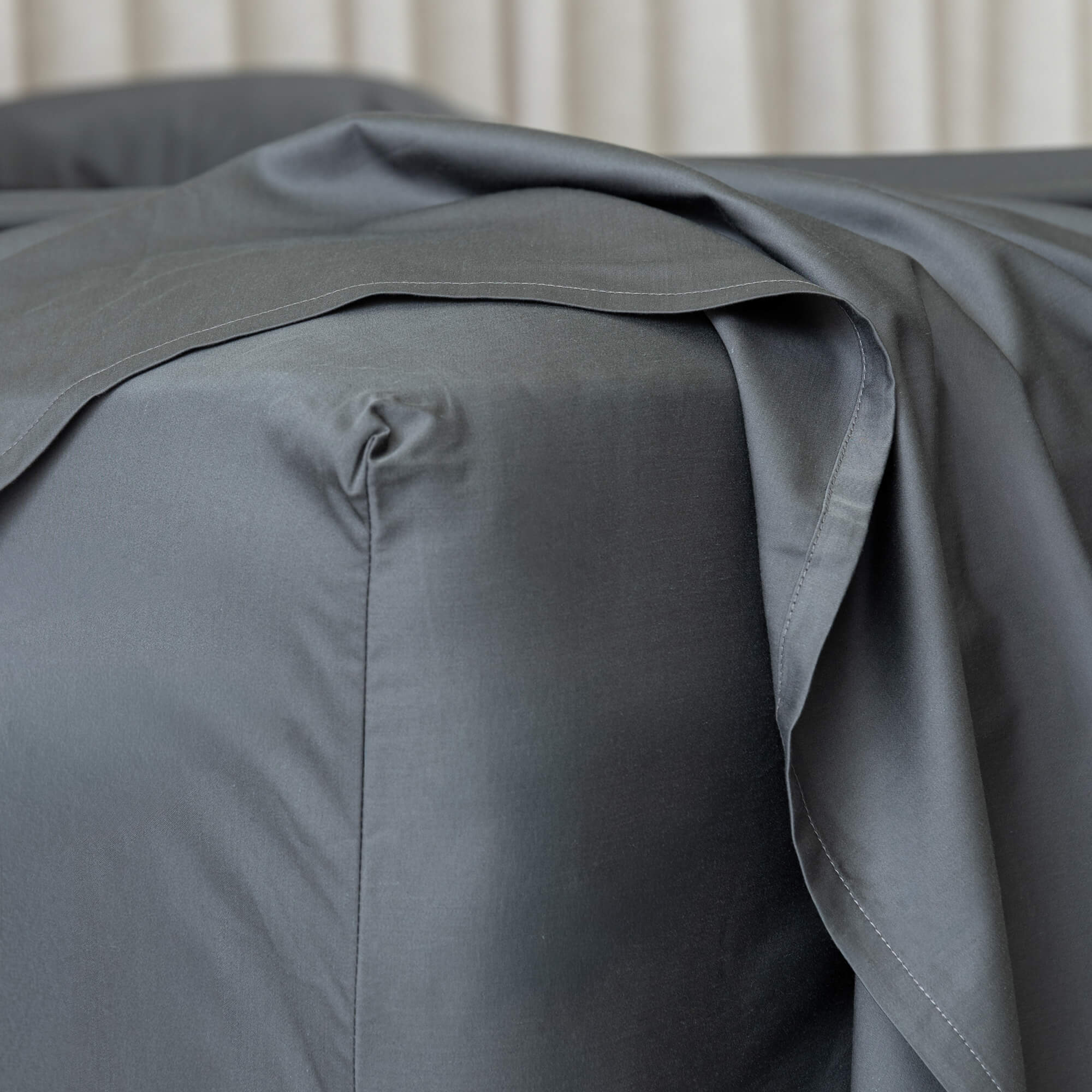 Charcoal grey fitted sheet on a bed, zoomed in on the corner. 