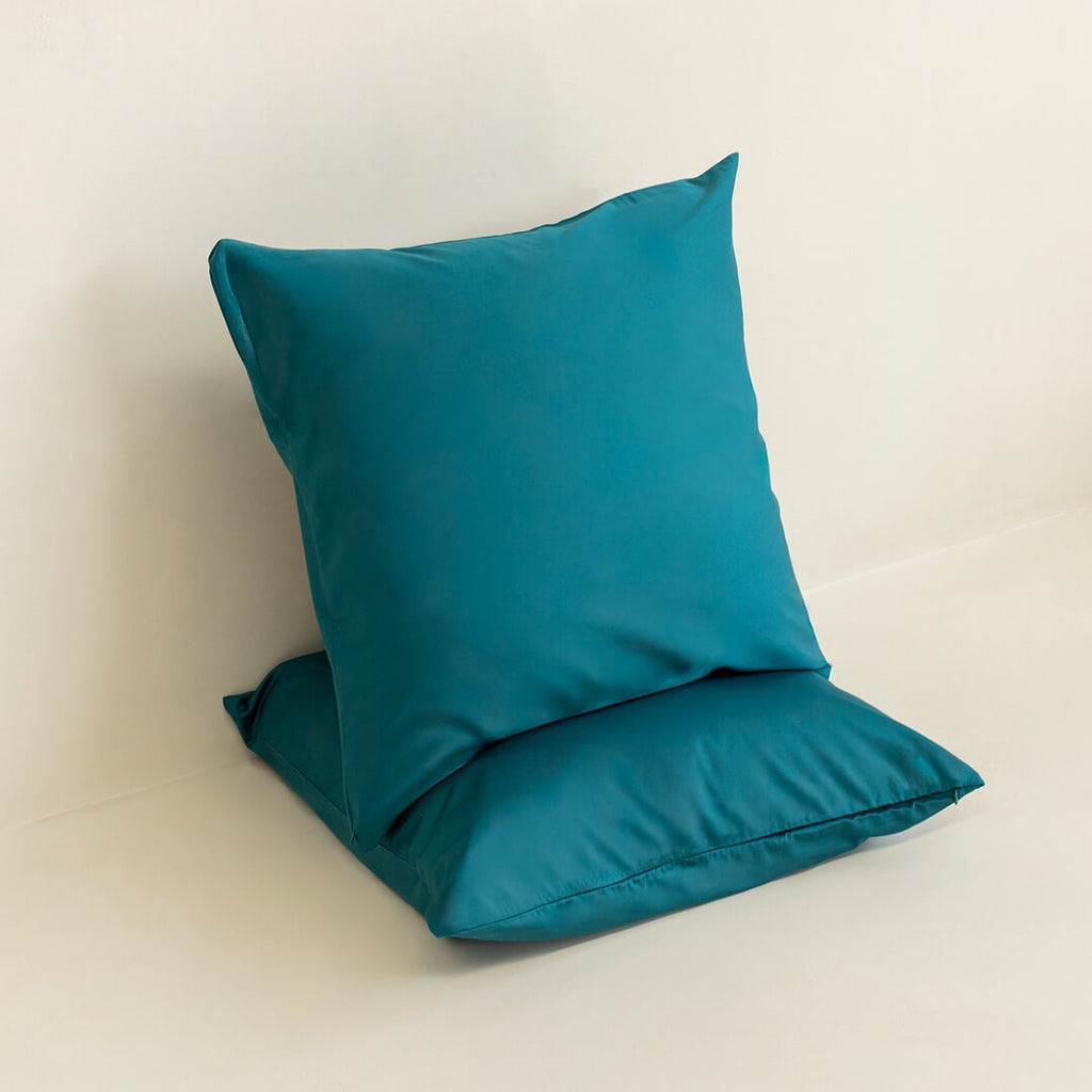 Two teal European pillowcases against a neutral background. 