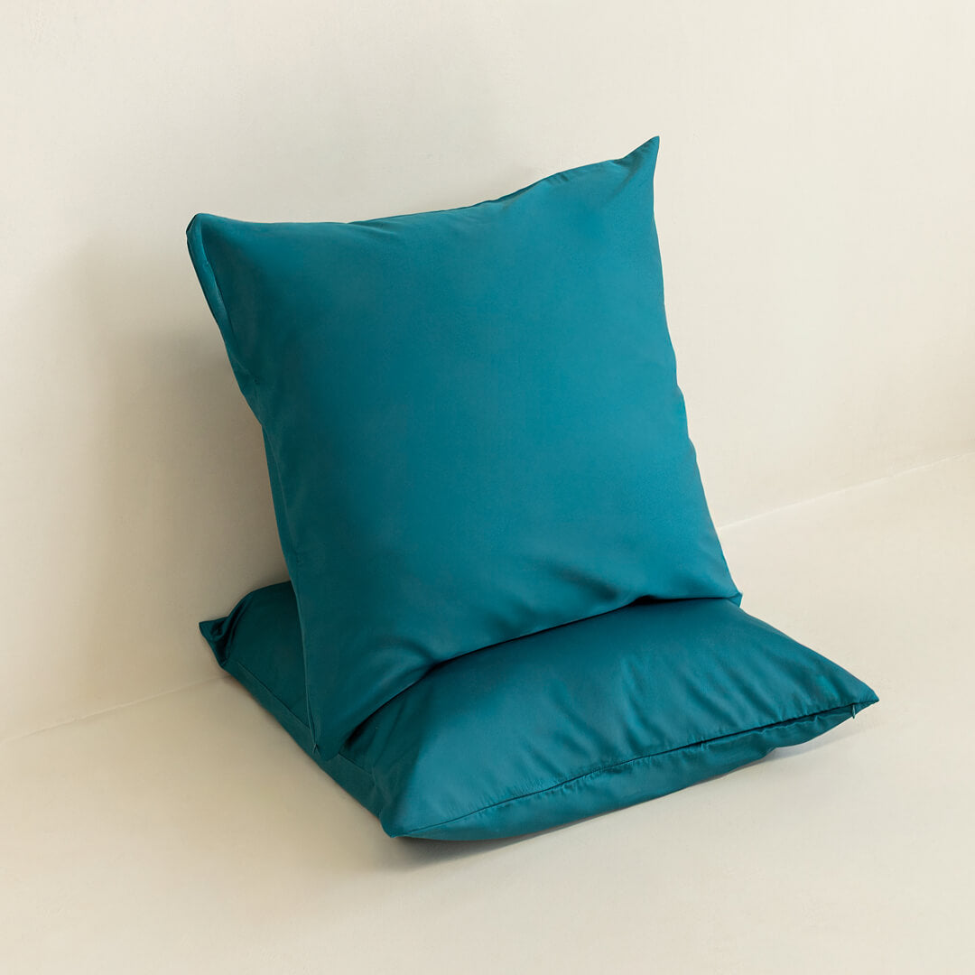 Two teal European pillowcases against a neutral background. 
