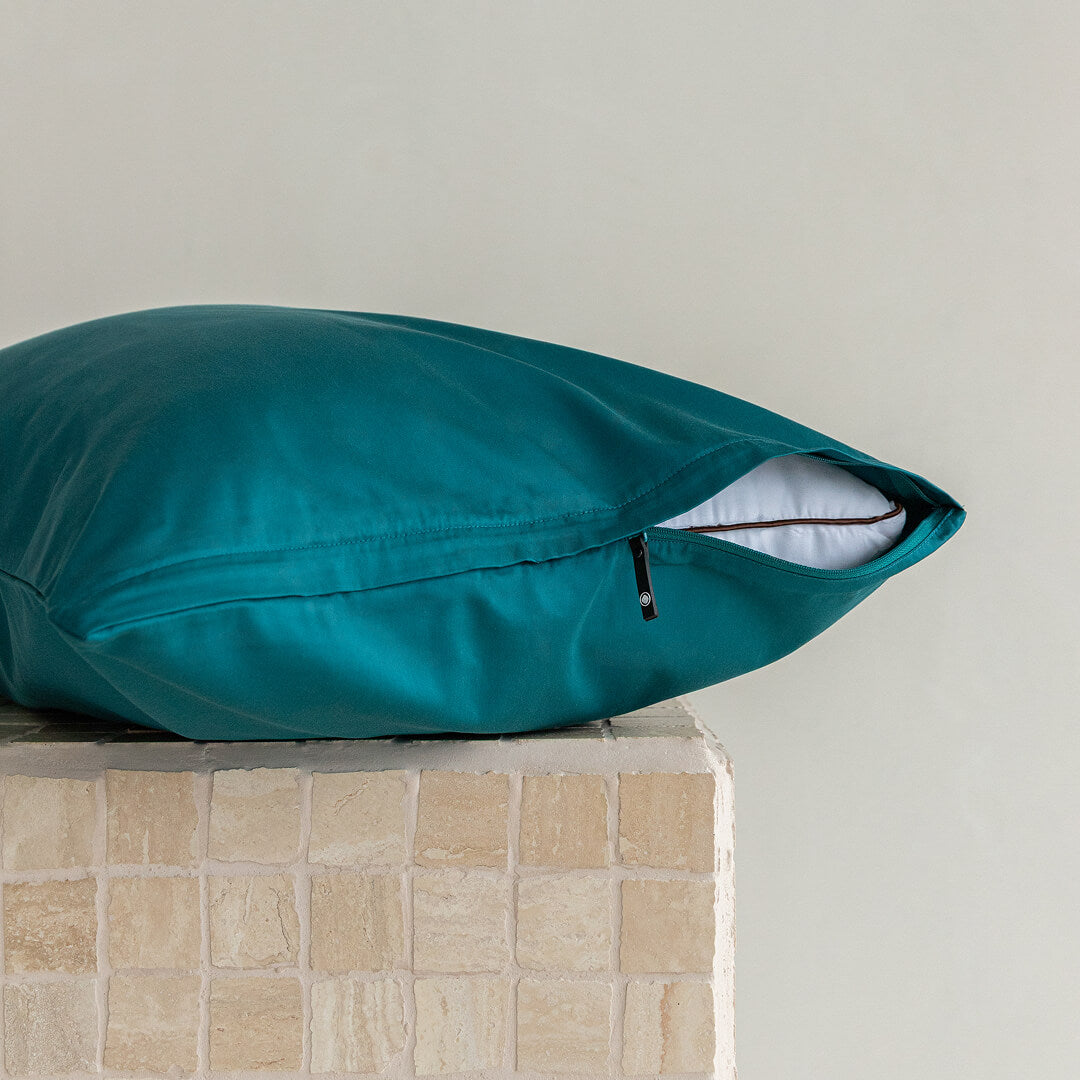 Pillow and teal pillowcase with invisible zipper on a textured surface with a neutral background.