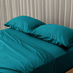 Teal bedspread on a bed with pillows against a beige curtain background