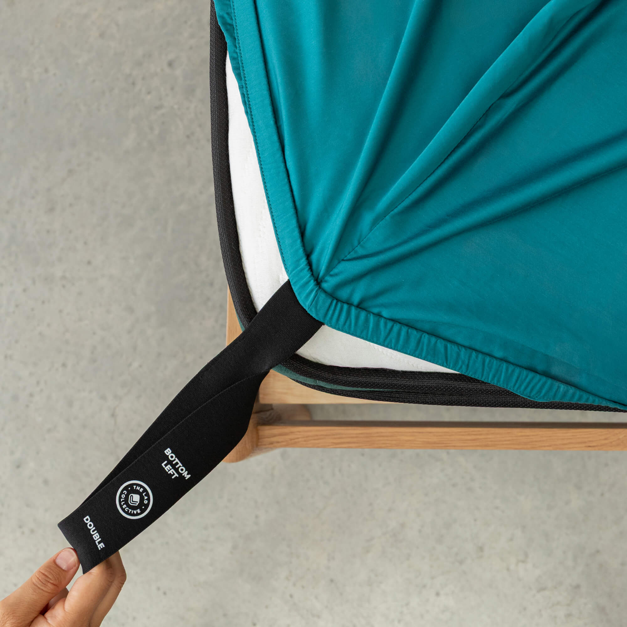 Person adjusting a teal fitted sheet with a black strap on a gray surface