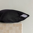Black pillow on a textured surface with a neutral background, showcasing the half open invisible zip on the pillowcase.