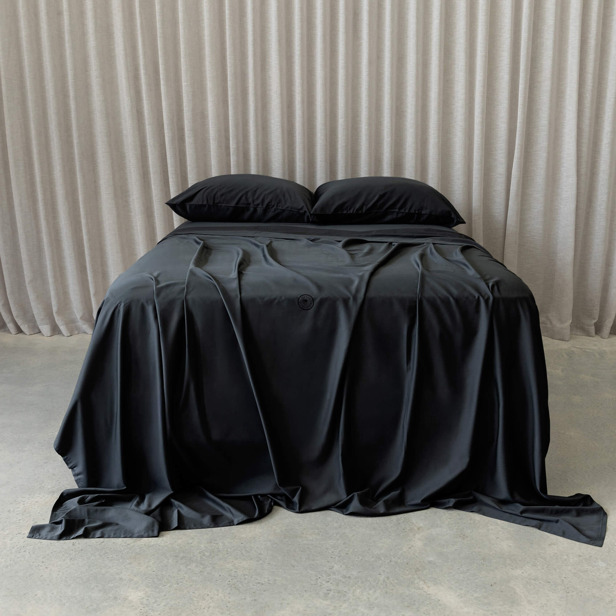 Black bed sheets on a bed with a neutral background