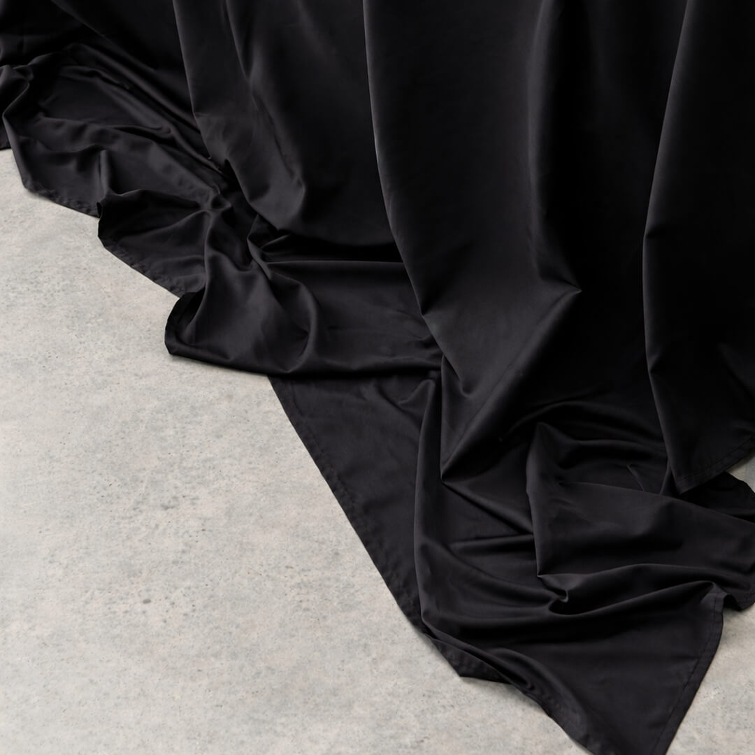 Black sheet draped over a bed on a light concrete floor.
