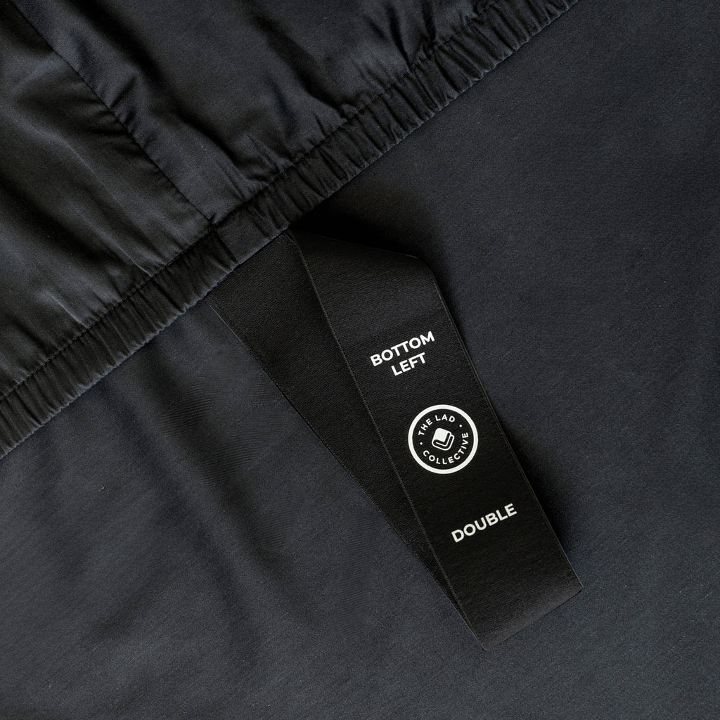 Close up of Black bed sheets with corner strap on a bed with a neutral background
