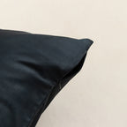 Black pillow on a beige background, showcasing zipper closure.