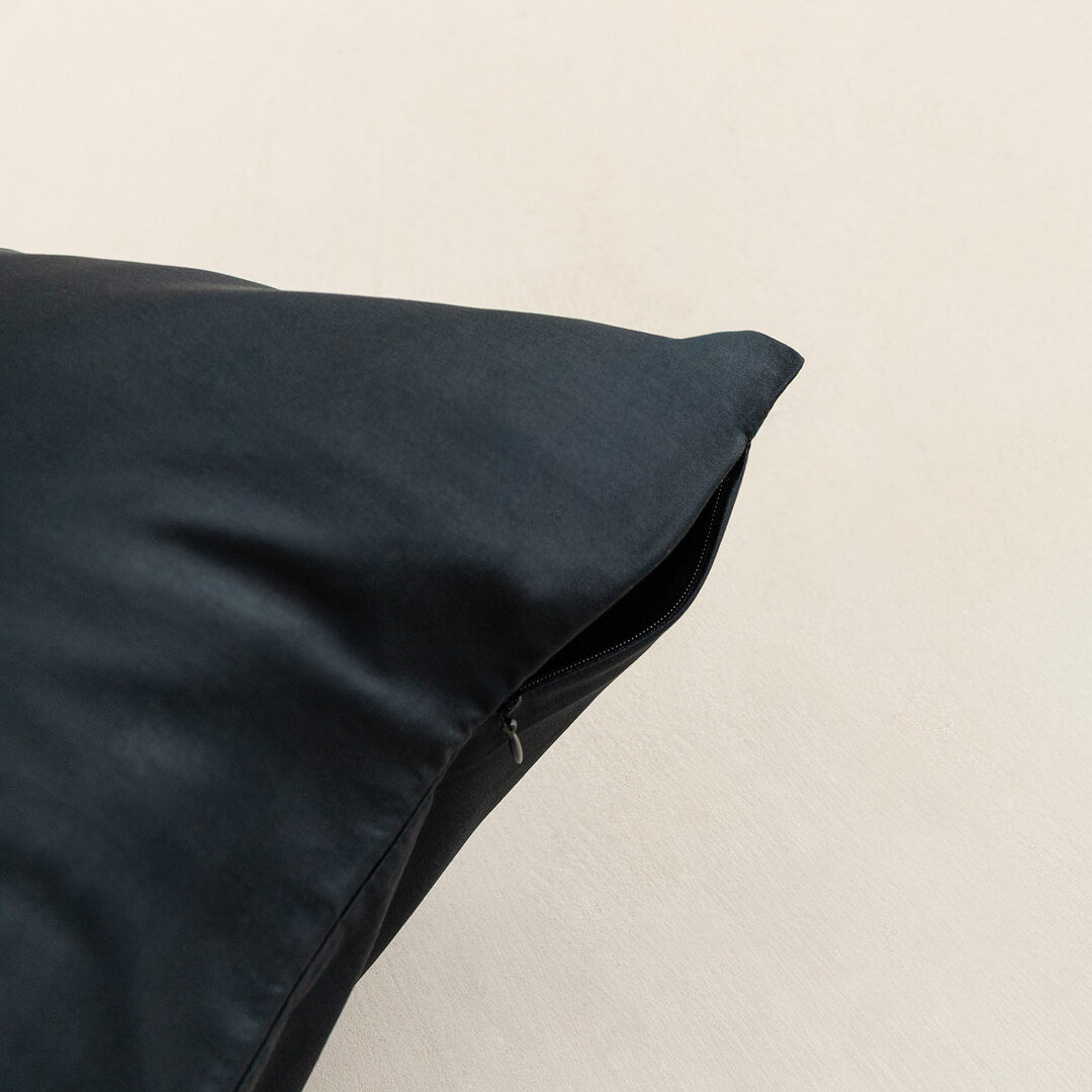 Black pillow on a beige background, showcasing zipper closure.