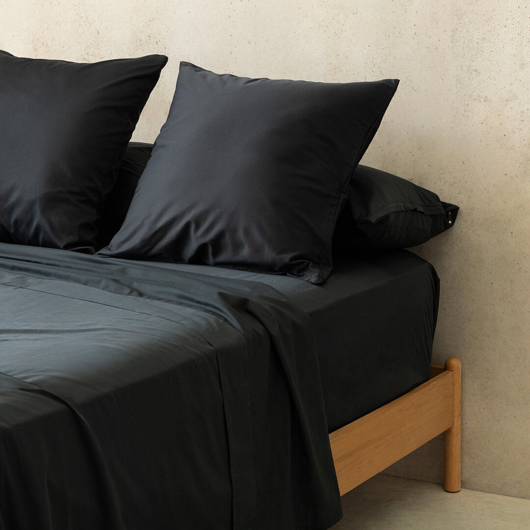 Black bedding set on a bed with a wooden headboard against a beige wall.
