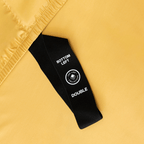 Close-up of a black corner elastic strap on a golden yellow fitted sheet printed with 'Bottom Left' position label