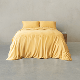 Golden yellow quilt cover set made up on a double bed with two matching pillowcases against a concrete wall