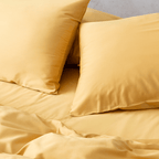 Close-up angle view of two golden yellow pillowcases and a flat sheet on a bed