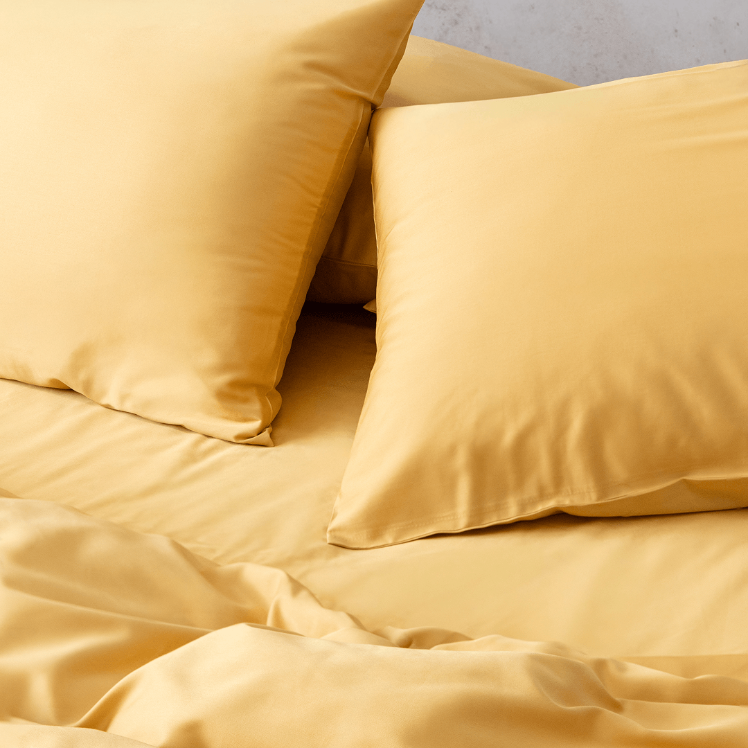 Close-up angle view of two golden yellow pillowcases and a flat sheet on a bed