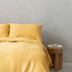 Front view of golden yellow quilt bedding set next to a wooden side table with a decorative object