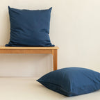 Two blue pillows on a wooden bench against a beige wall.