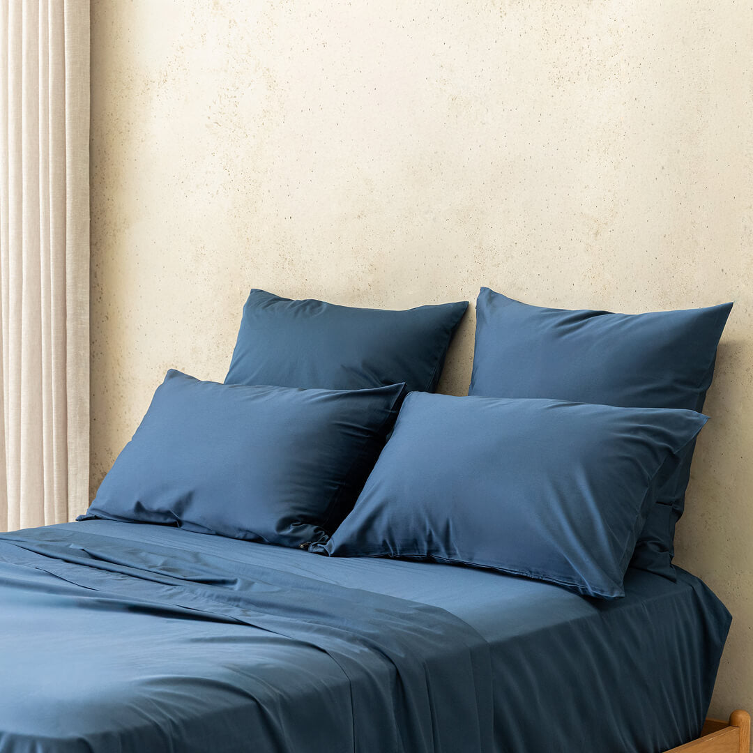 Blue bedding set with pillows on a bed against a beige wall.