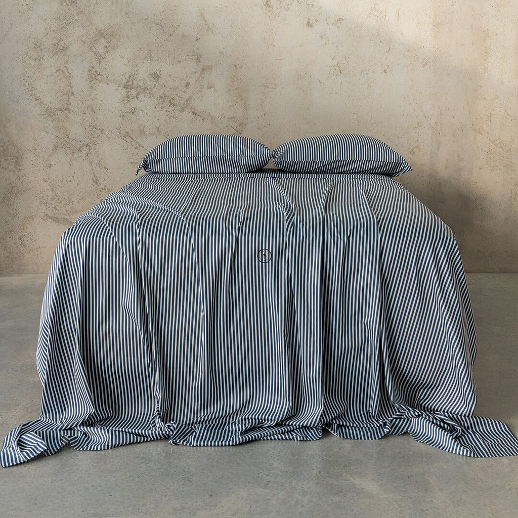 Striped bedspread and pillows on a bed against a textured wall.