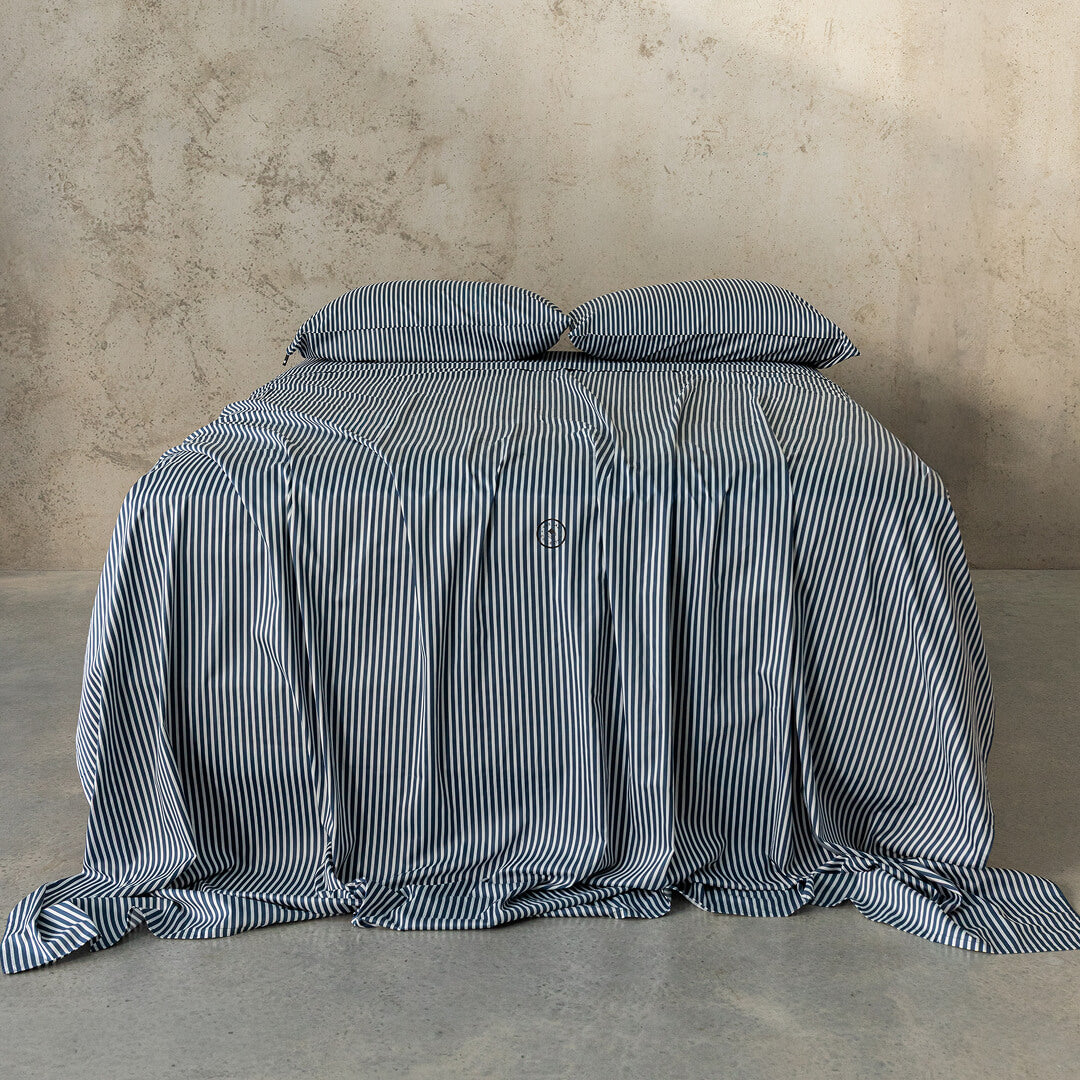 Striped bedspread and pillows on a bed against a textured wall.