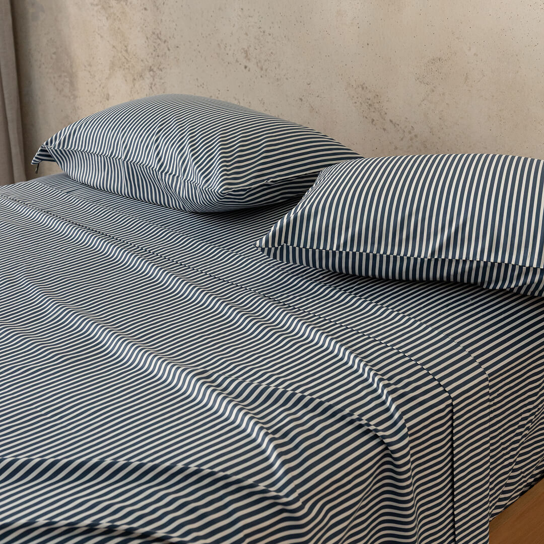 Striped bedspread and pillows on a bed against a neutral wall.