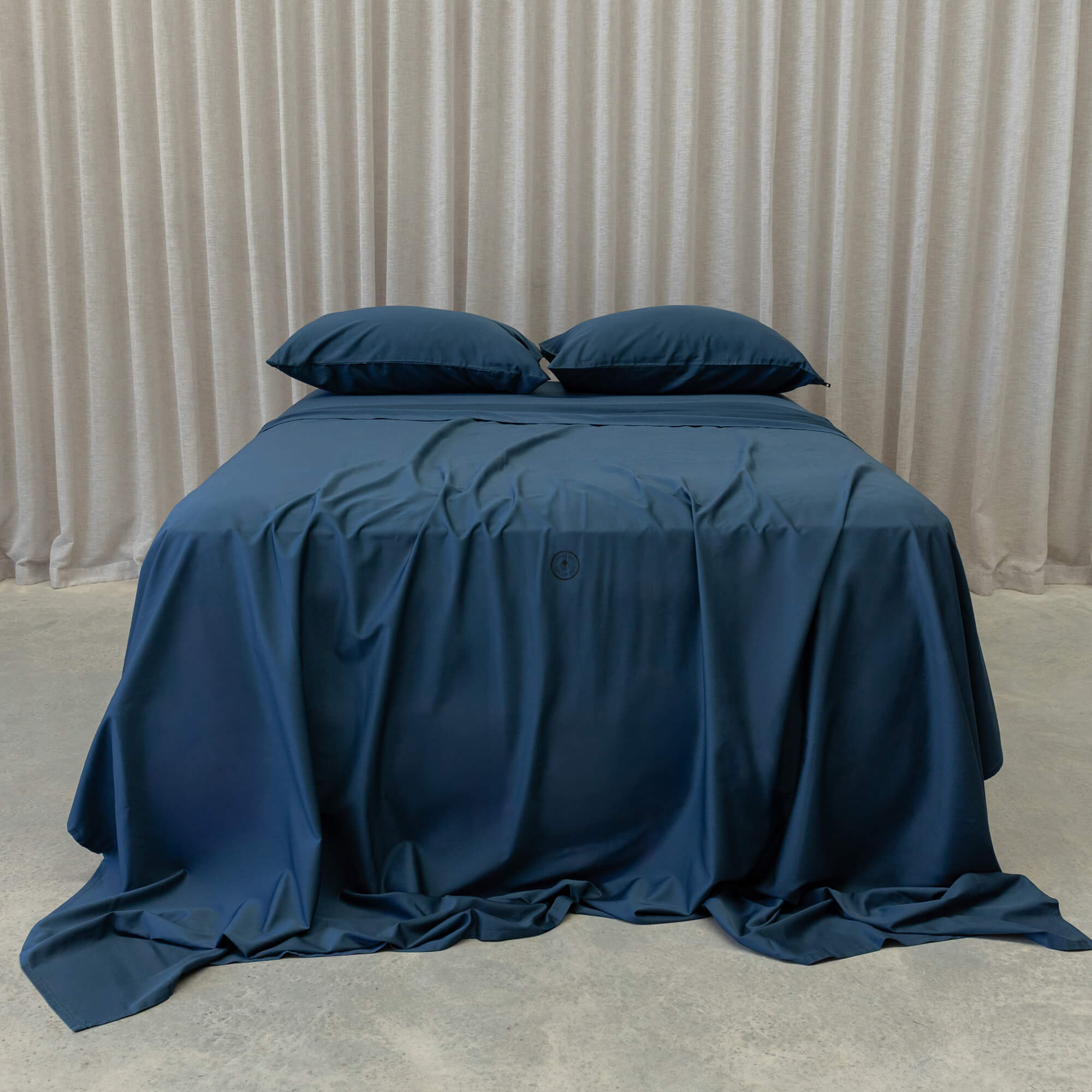 Blue bedspread on a bed with pillows against a beige curtain background
