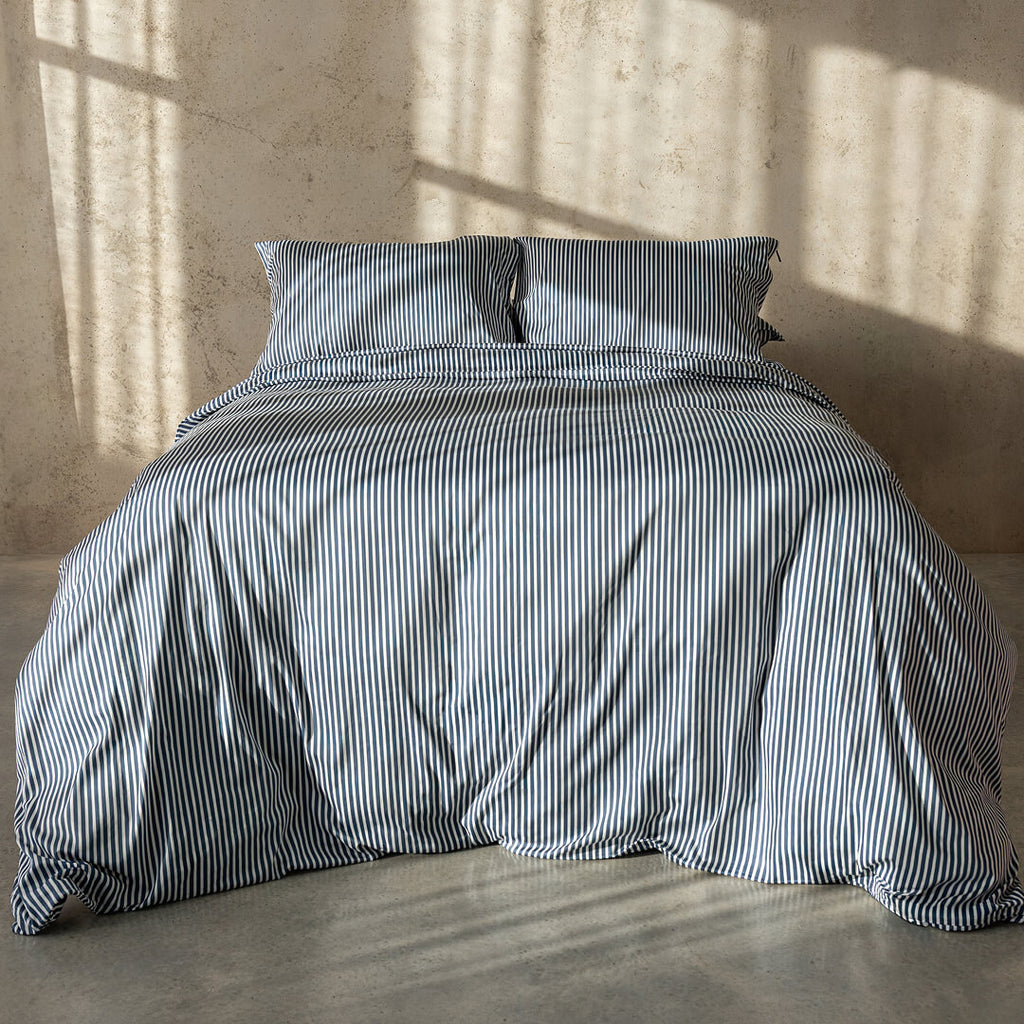 Striped bedspread and pillows on a bed with a neutral wall and floor background.