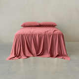Dusty rose pink bed sheet set draped over a double bed with two matching pillowcases against a neutral wall