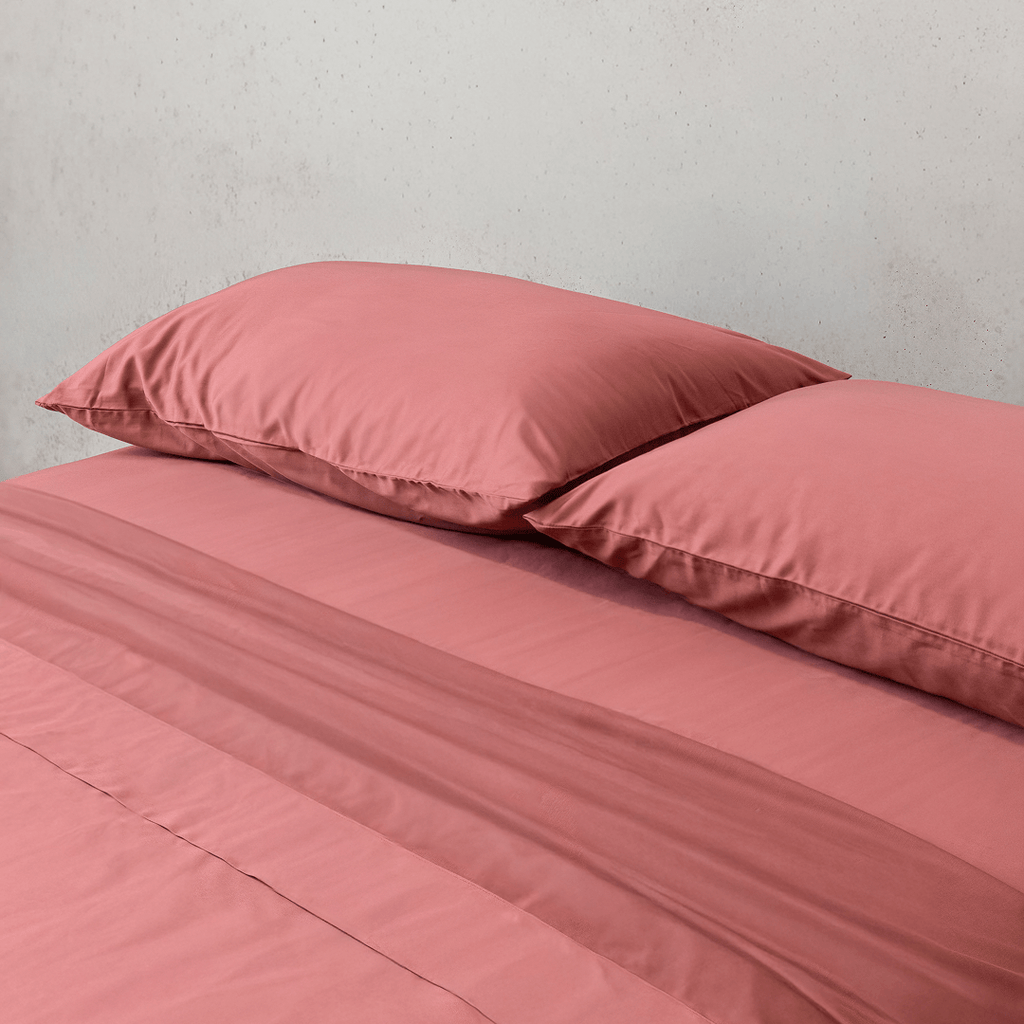 Angle view of two dusty rose pink pillowcases and a matching flat sheet neatly arranged on a bed