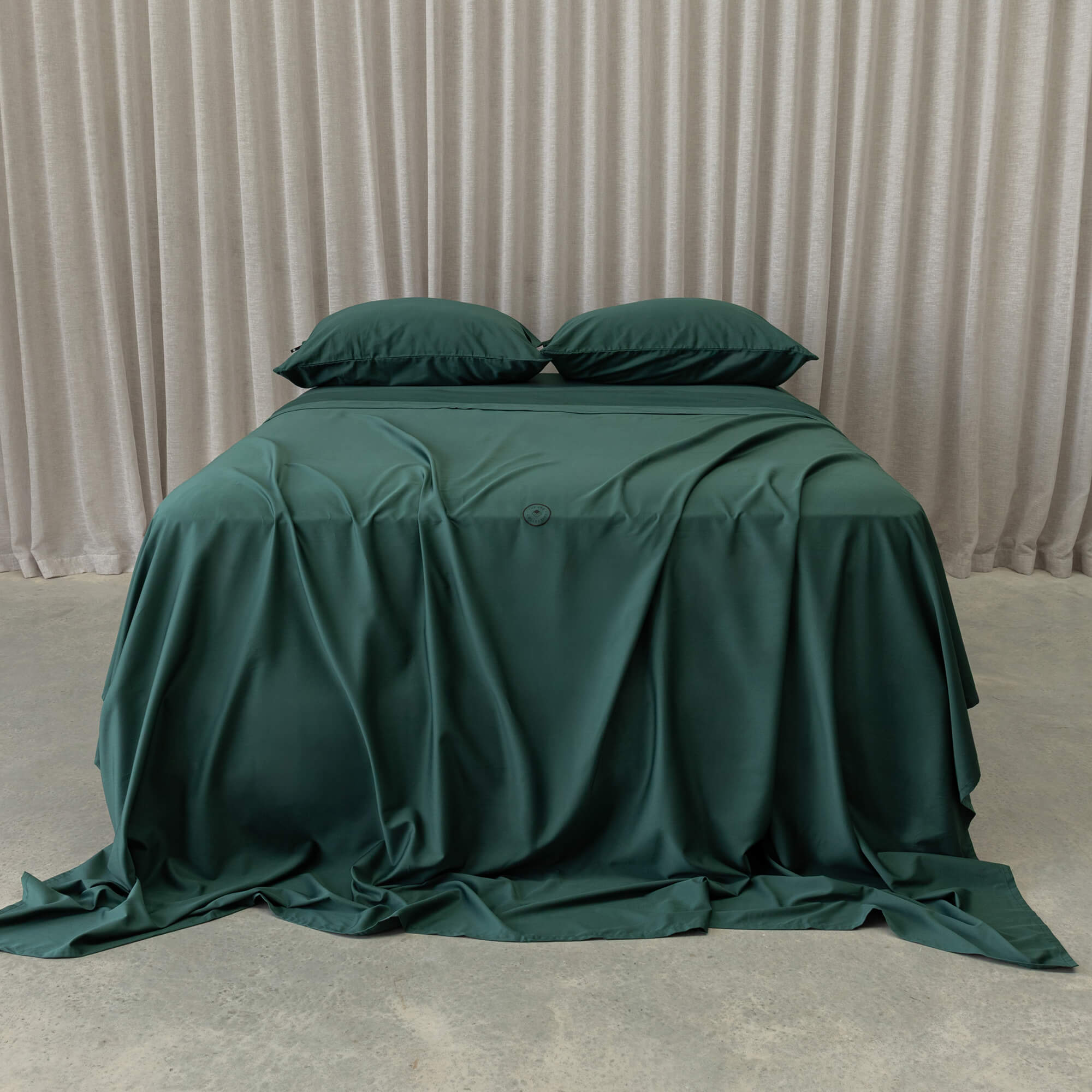 Green bedspread and pillows on a bed with beige curtains in the background