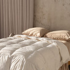 Beige quilt insert and pillows on a bed with a neutral wall and curtain in the background.