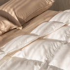 Beige comforter and pillows on a bed with a neutral background.