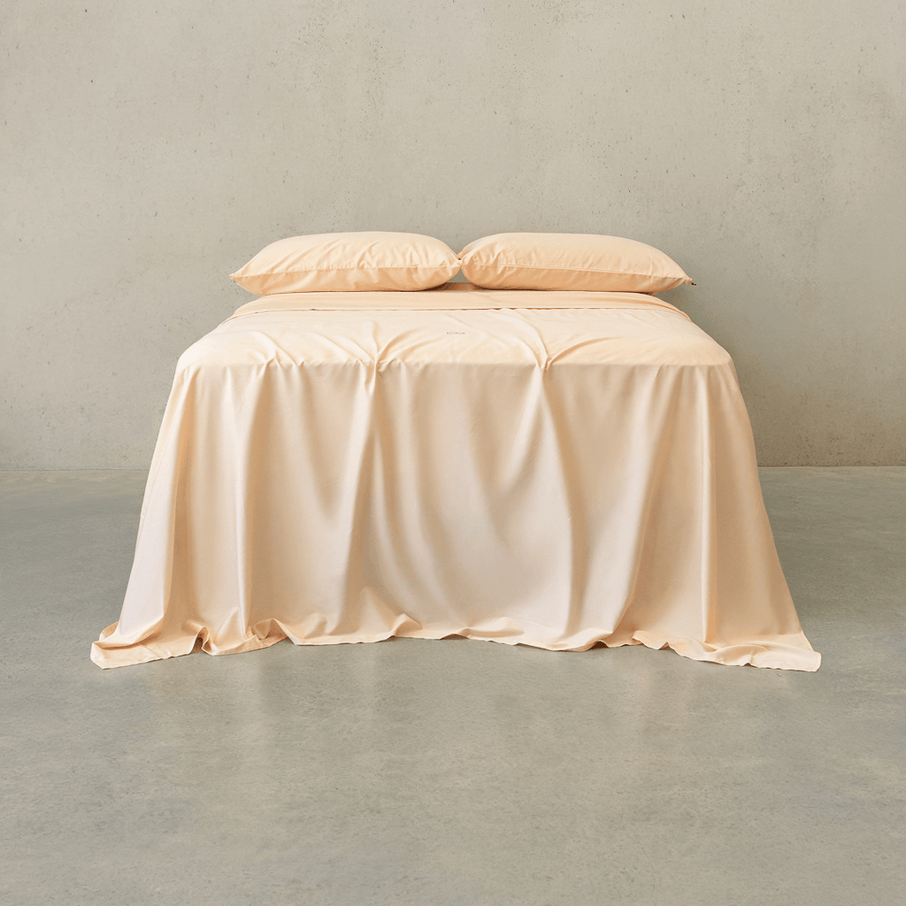 Peach-colored bed sheet set draped over a double bed with two matching pillowcases against a neutral wall
