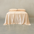 Peach-colored bed sheet set draped over a double bed with two matching pillowcases against a neutral wall