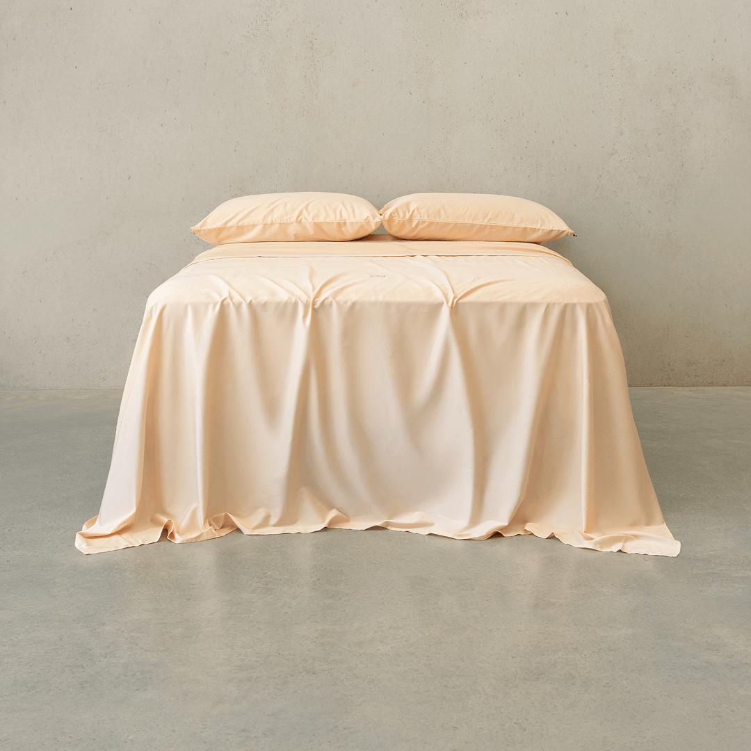 Peach-colored bed sheet set draped over a double bed with two matching pillowcases against a neutral wall