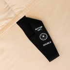 Close-up of a black corner elastic strap on a peach fitted sheet printed with 'Bottom Left' position label